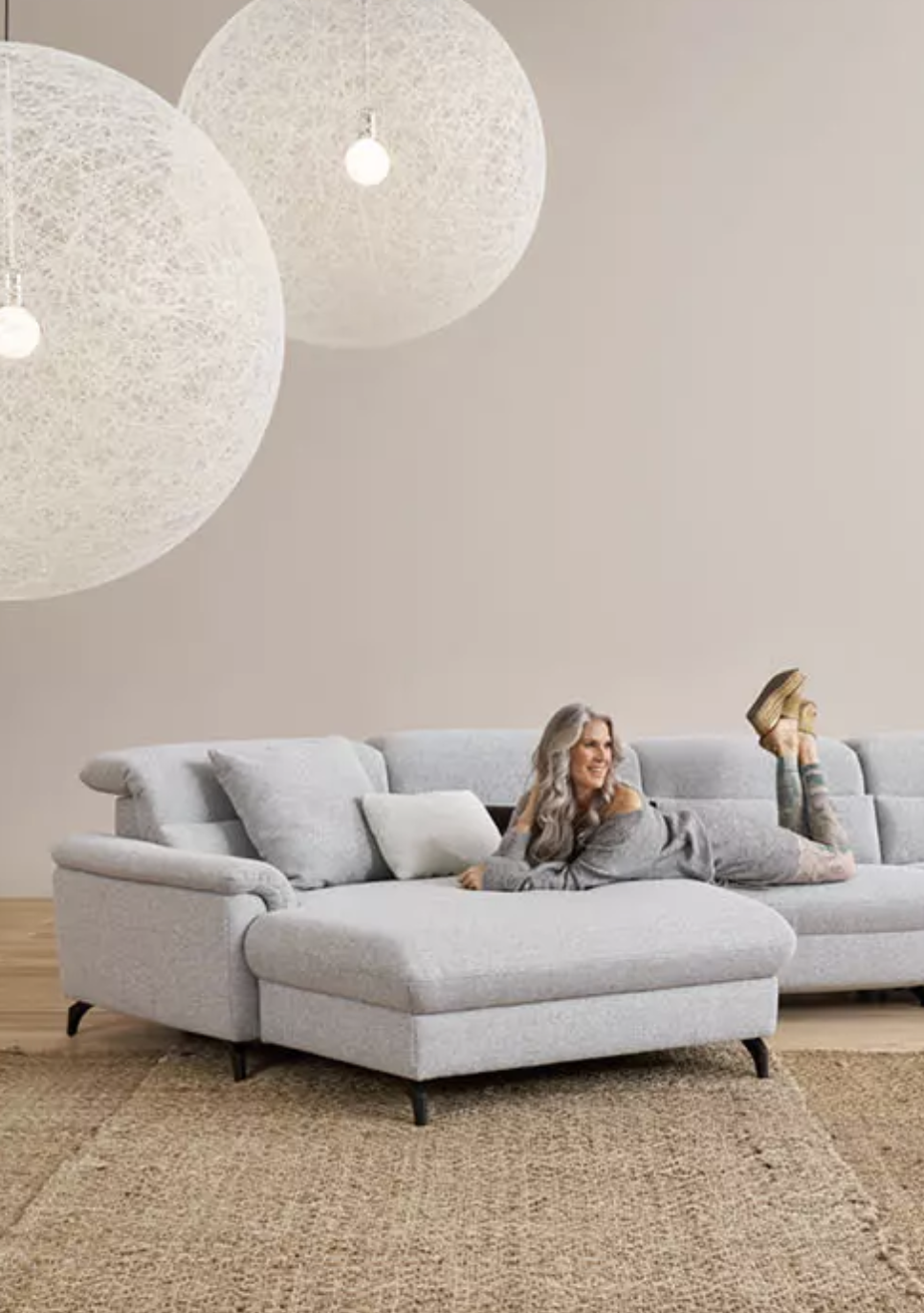 Modernes, minimalistisches Wohnzimmer mit grauem Ecksofa, Hängelampen und entspannter Person