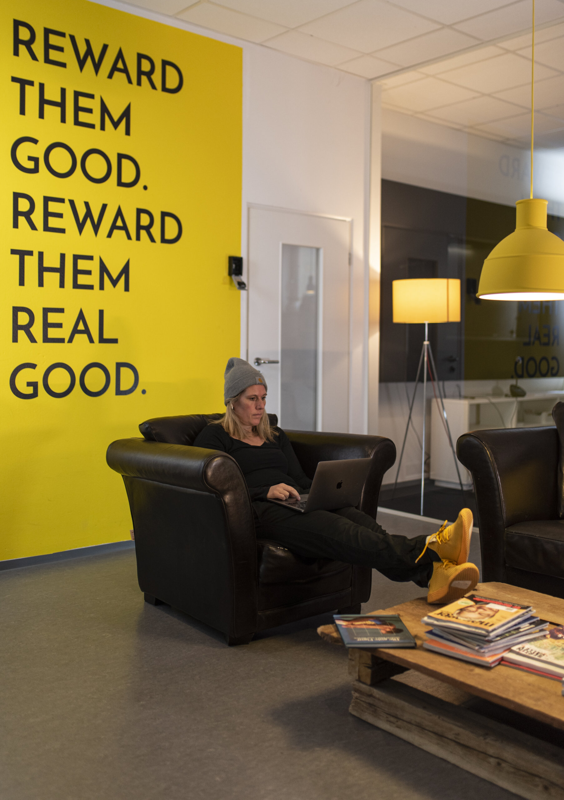 Moderne Büro-Lounge mit gelber Sloganwand, Lederstühlen und entspanntem Meetingbereich