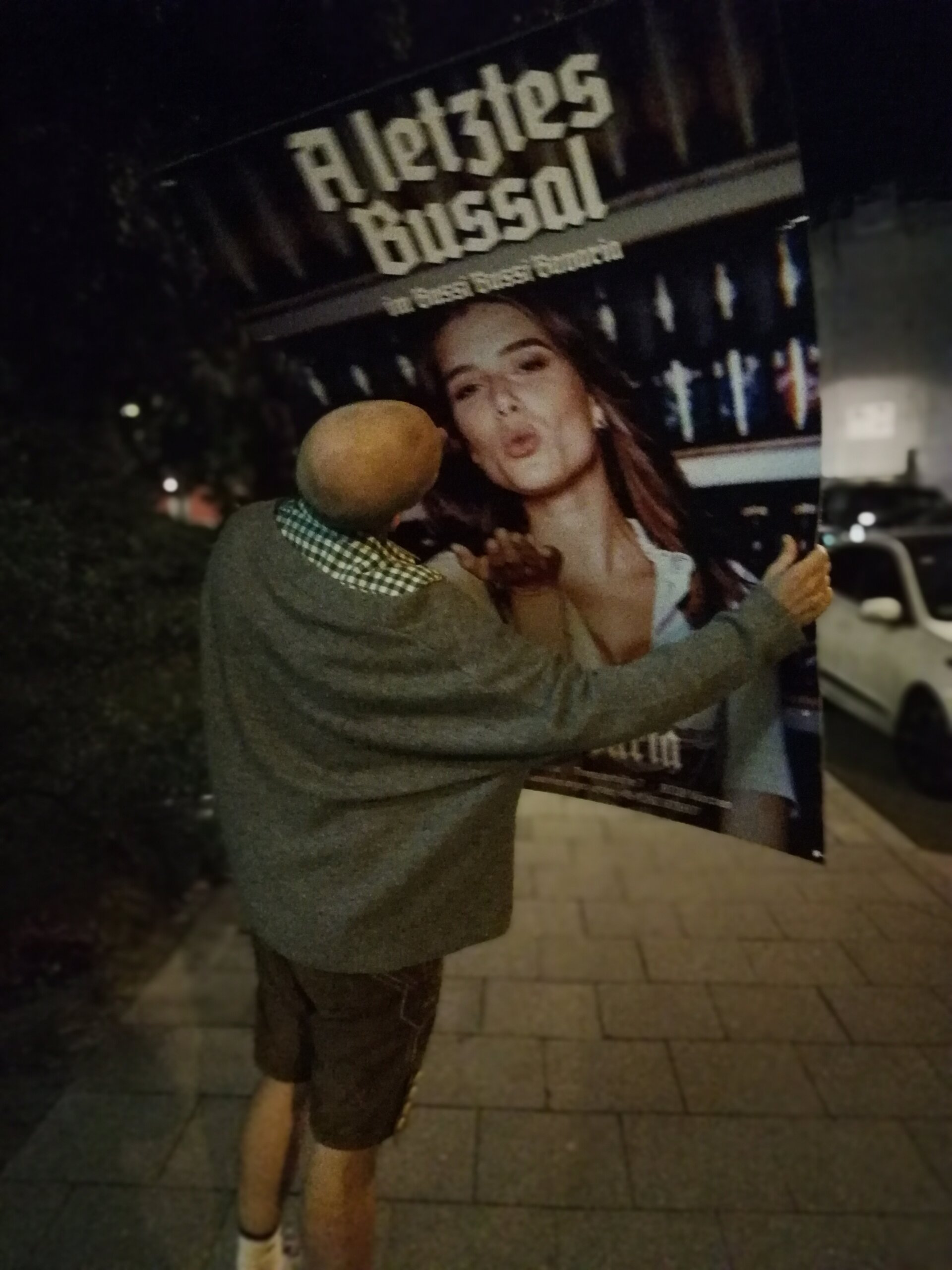 Person küsst leuchtendes Werbeplakat auf städtischem Gehweg bei Nacht