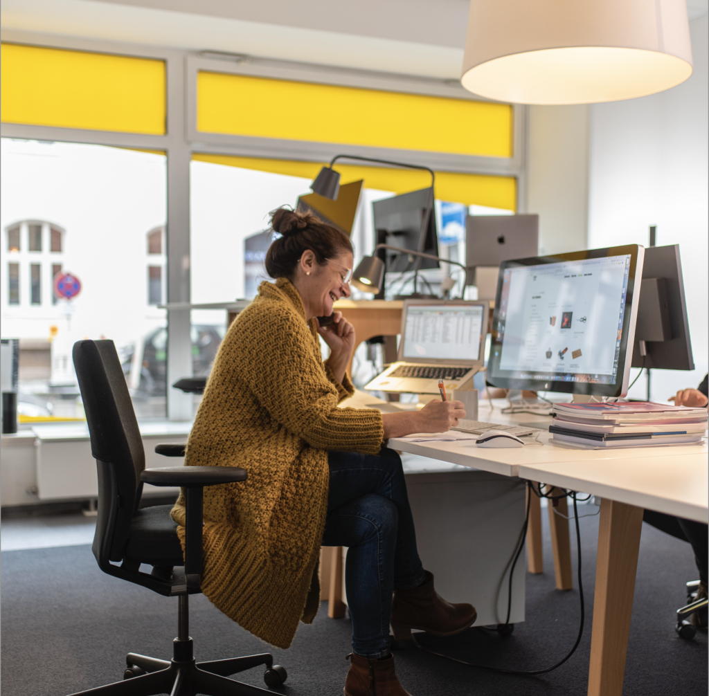 Konzentrierte Mitarbeiterin am Laptop im modernen Büro mit gelben Rollos