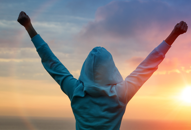 Person im Hoodie bei Sonnenaufgang mit erhobenen Fäusten: Triumph und Freiheit