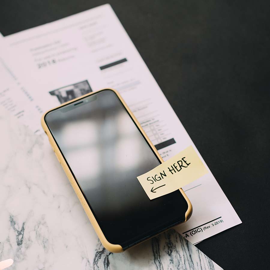 Smartphone mit Post-it SIGN HERE auf Dokumenten – Unterschrift erforderlich