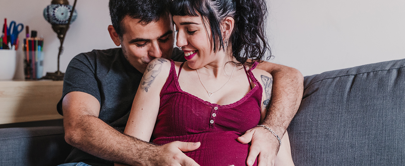 Liebevolles Paar umarmt Babybauch auf Sofa