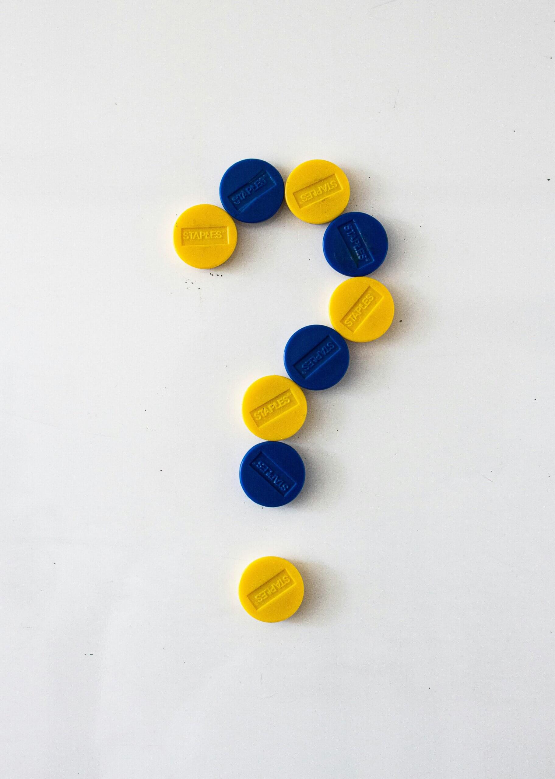 Spielerisches Fragezeichen aus blauen und gelben Plastikkappen auf weißem Hintergrund