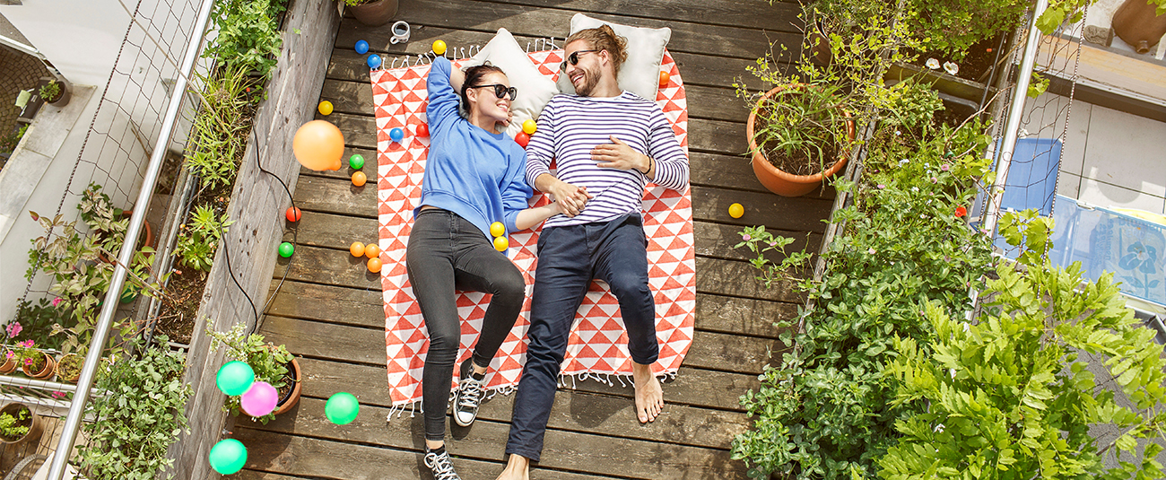 Paar auf karierter Picknickdecke auf sonniger Dachterrasse, umgeben von Pflanzen