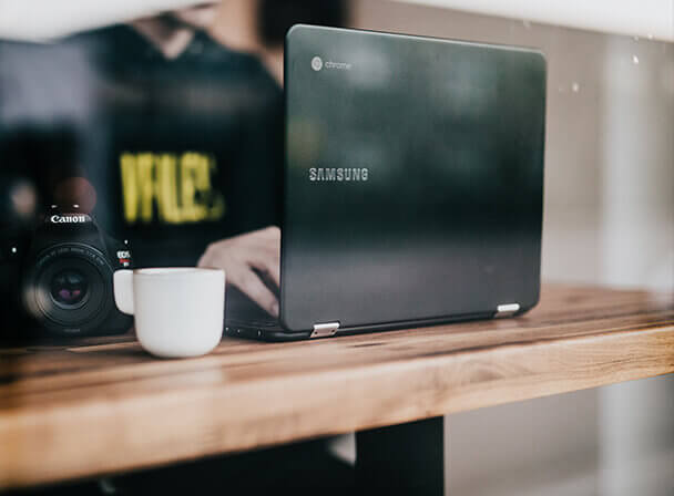 Samsung-Laptop, Canon-Kamera und Kaffee auf Holztheke im Café — mobiles Arbeiten