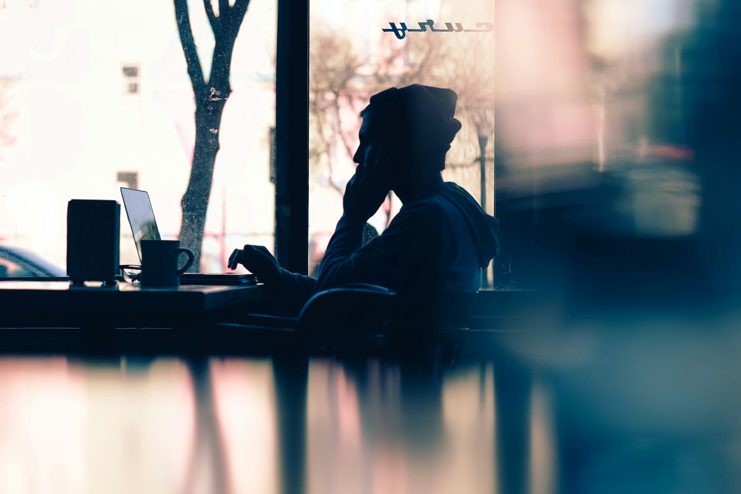 Silhouette am Caféfenster mit Laptop und Handy – urbaner Arbeitsmoment