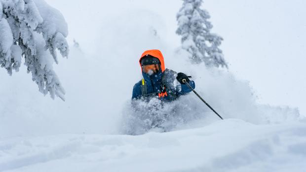 Skifahrer im Tiefschnee mit orangefarbener Kapuze und fliegendem Pulverschnee