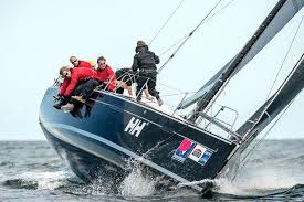 Segelboot Sloop in Schräglage: Crew in roten Jacken gegen Wind und Wellen