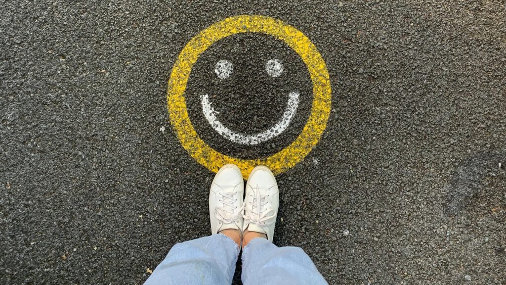 Weiße Sneaker vor gelbem Smiley auf Asphalt, Draufsicht