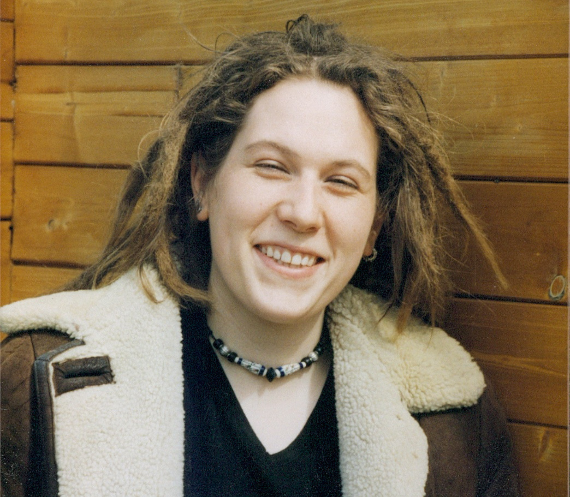 Lächelndes Porträtfoto mit Dreadlocks vor warmer Holzwand