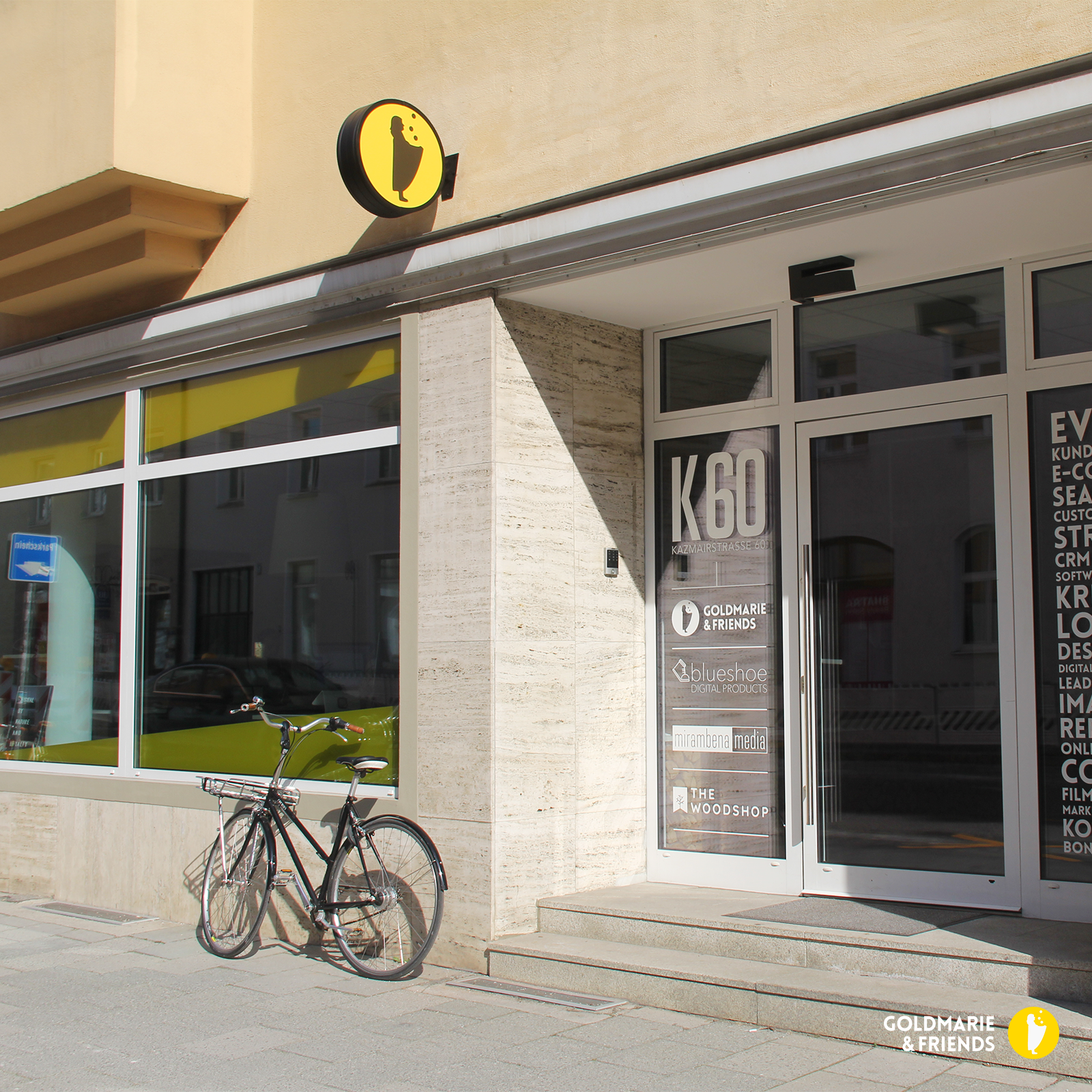 Modernes Schaufenster mit gelbem K80‑Logo, Glasfront und geparktem Fahrrad