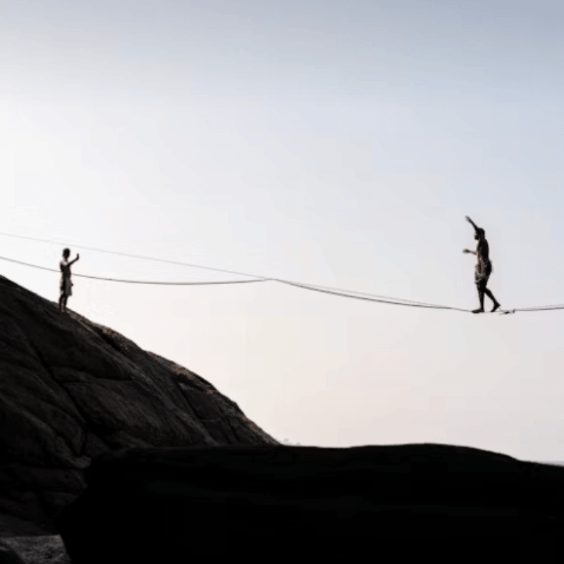 B2B Empfehlungsmarketing: Balanceakt auf Drahtseil zwischen Felsen, zwei Silhouetten