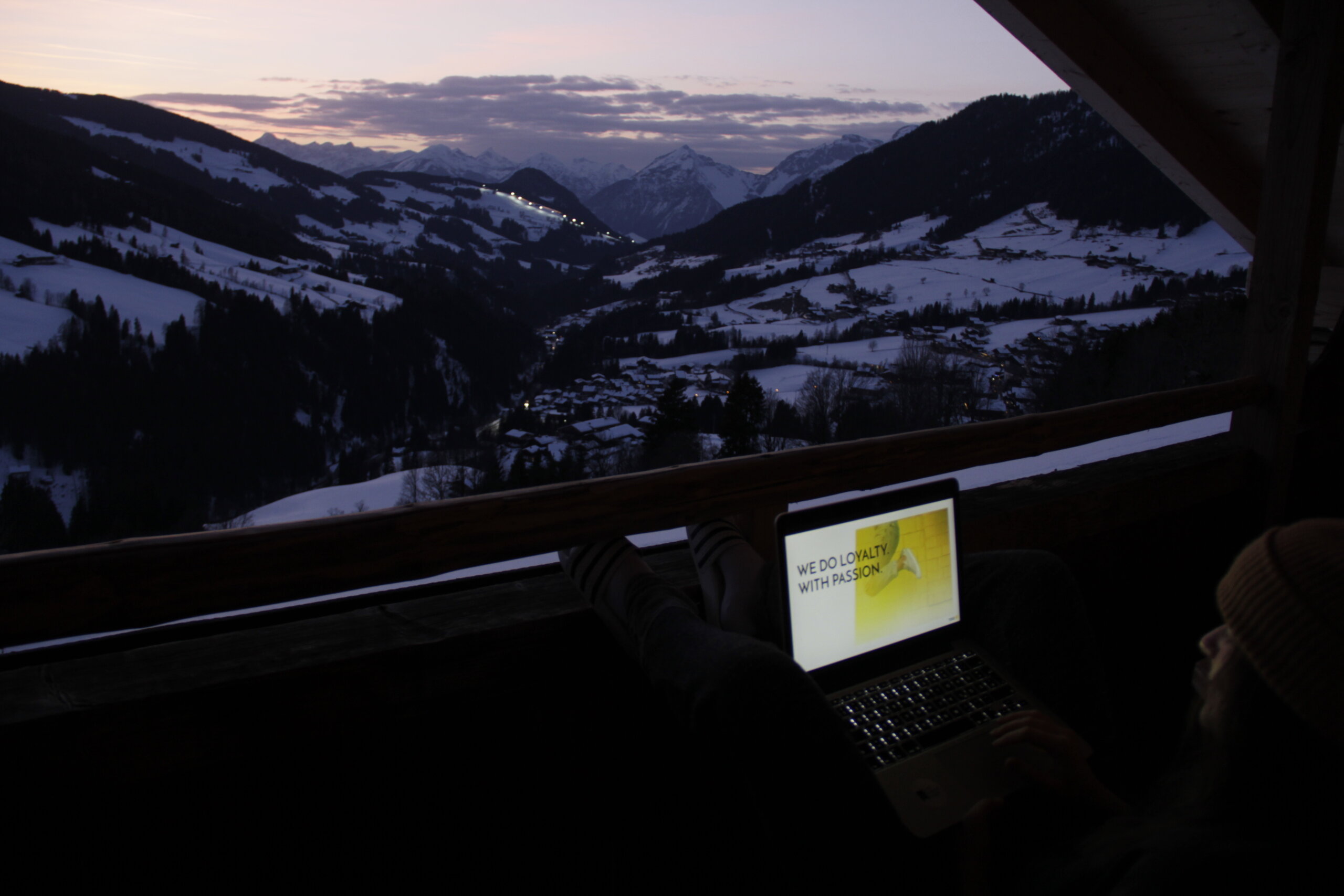 Laptop auf Balkon, Blick ins schneebedeckte Wintertal bei Dämmerung