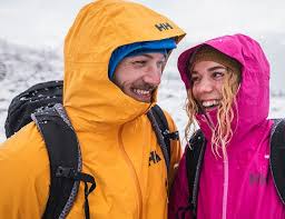 Zwei lachende Winterwanderer in bunten Jacken und mit Rucksäcken im Schnee