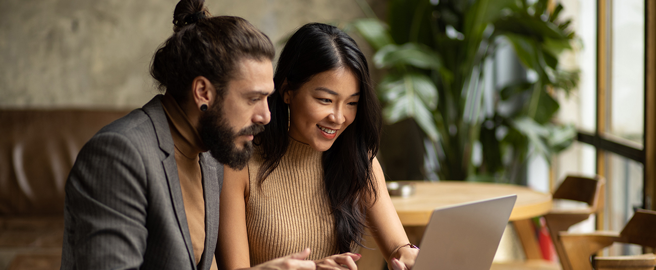 Zwei Kollegen arbeiten entspannt zusammen am Laptop in gemütlichem Café
