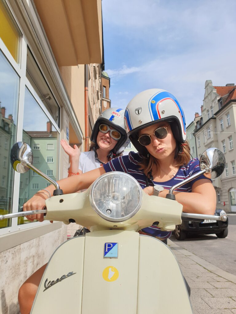 Paar auf cremefarbener Vespa in sonniger europäischer Altstadtgasse