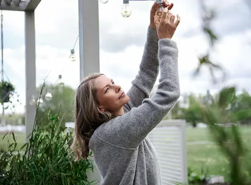 Frau hängt Lichterkette unter Pergola im Garten