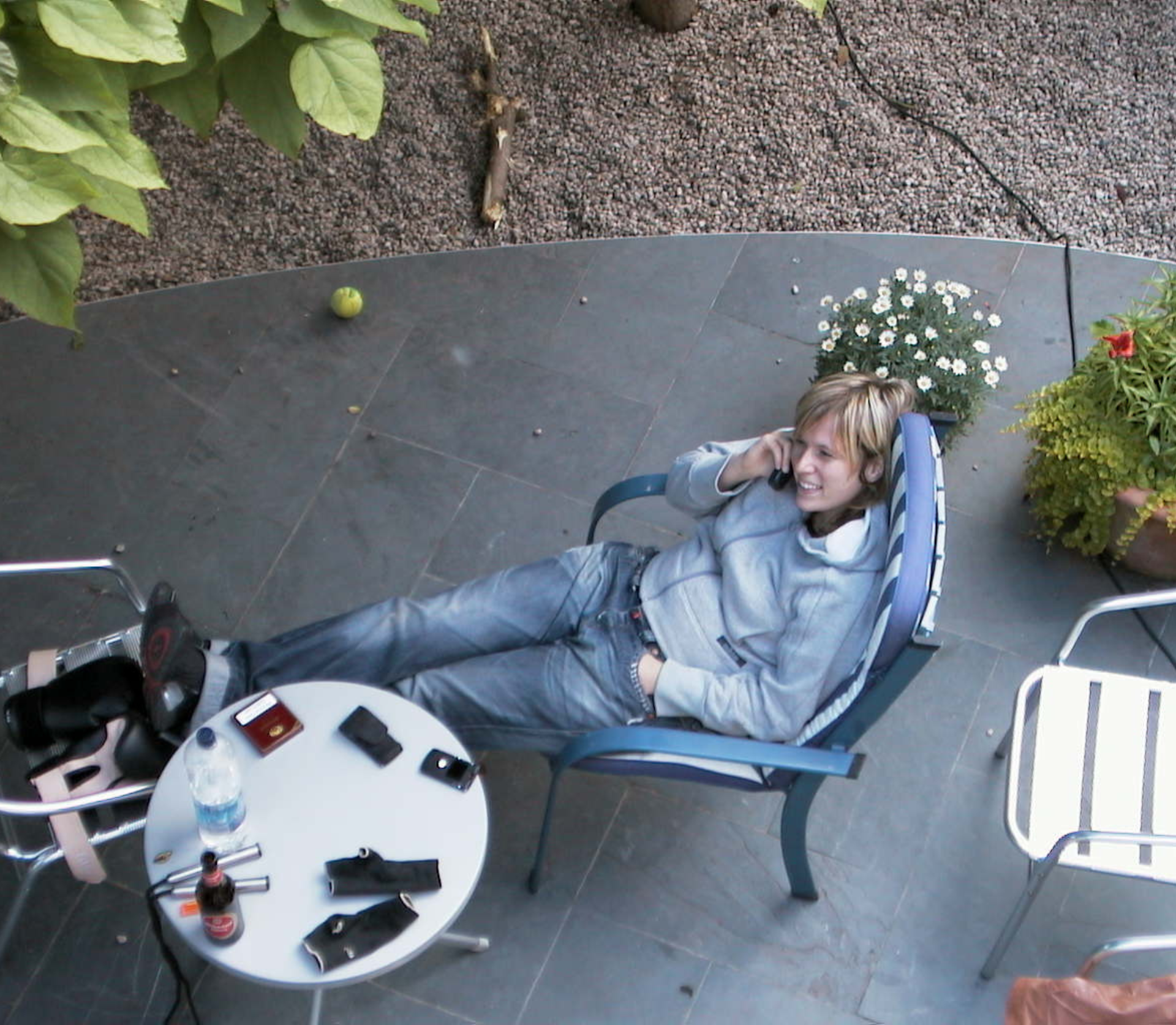 Entspannte Frau telefoniert im Liegestuhl auf ruhiger Terrasse mit Pflanzen