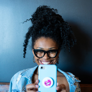 Lächelndes Selfie einer Frau mit Brille in Jeansjacke und blauem Handy