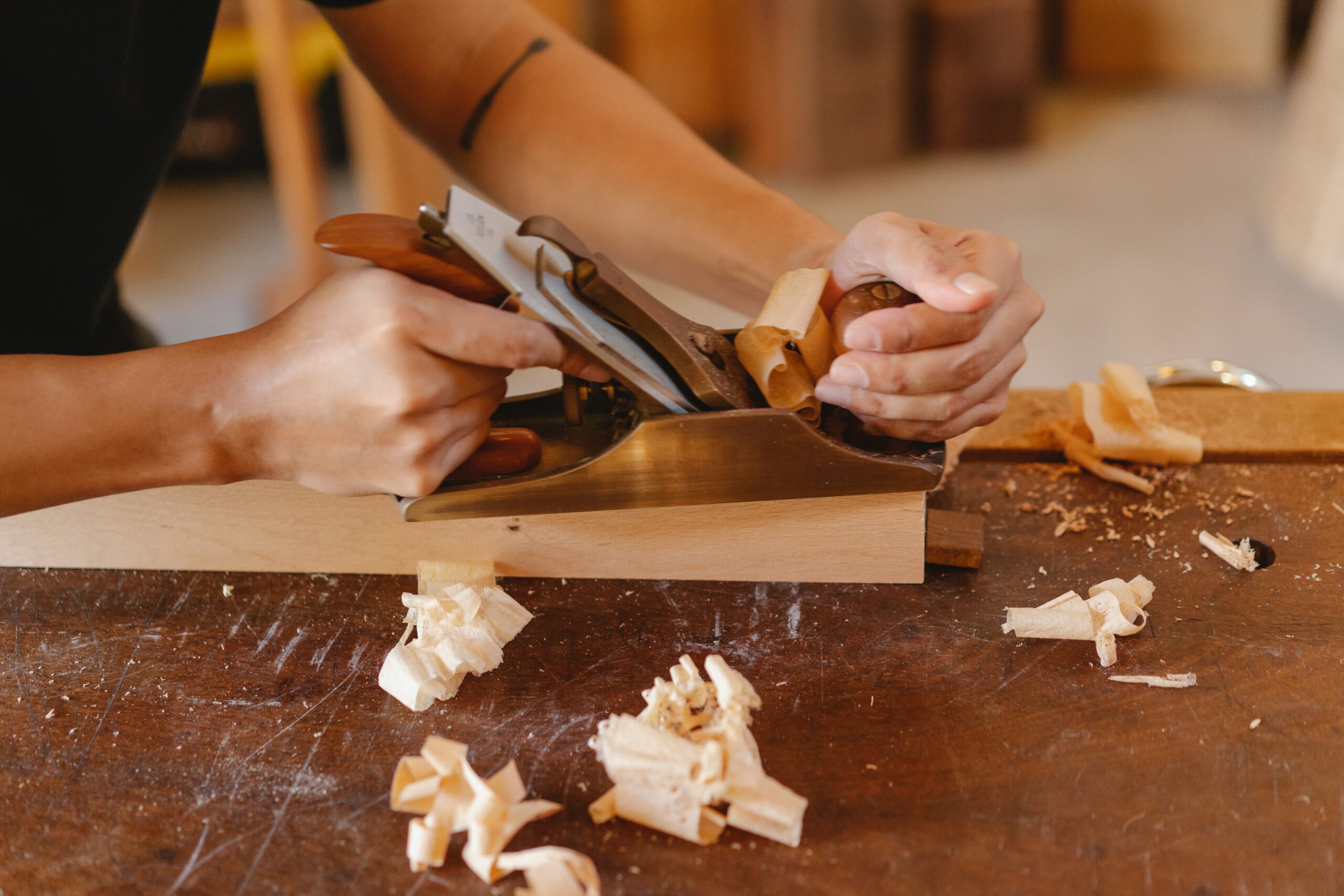 Handhobel auf Werkbank: Hände hobeln Holz, feine Späne, traditionelles Handwerk