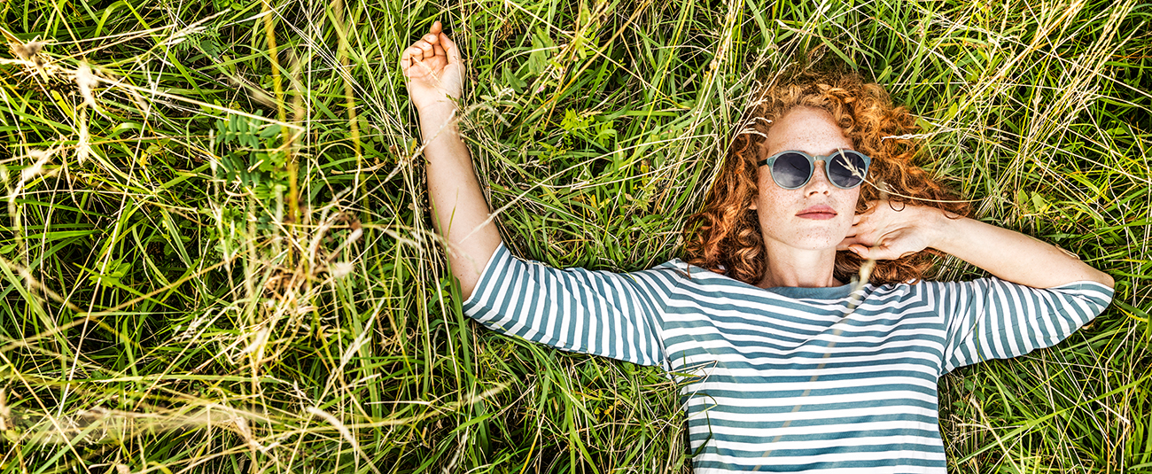 Frau liegend auf Sommerwiese mit roten Locken und Sonnenbrille